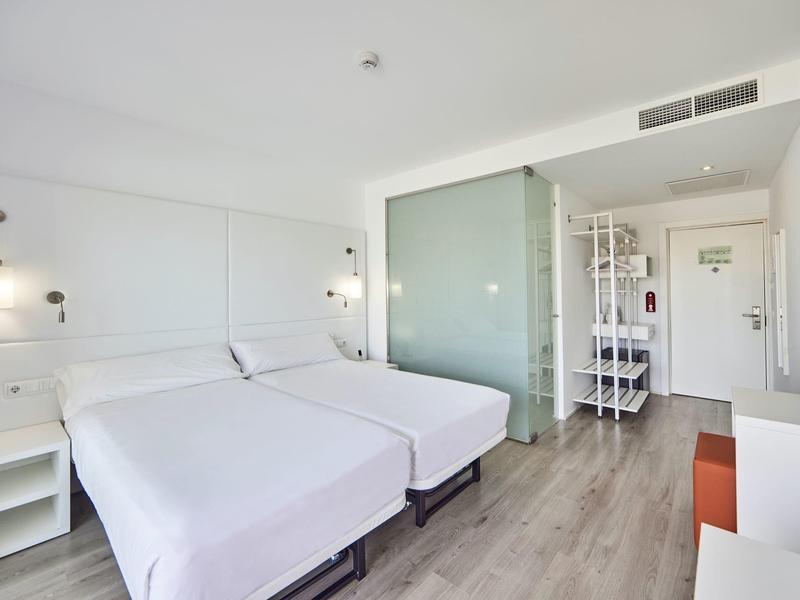 Habitación de hotel moderna con dos camas individuales, decoración blanca y suelo de madera.