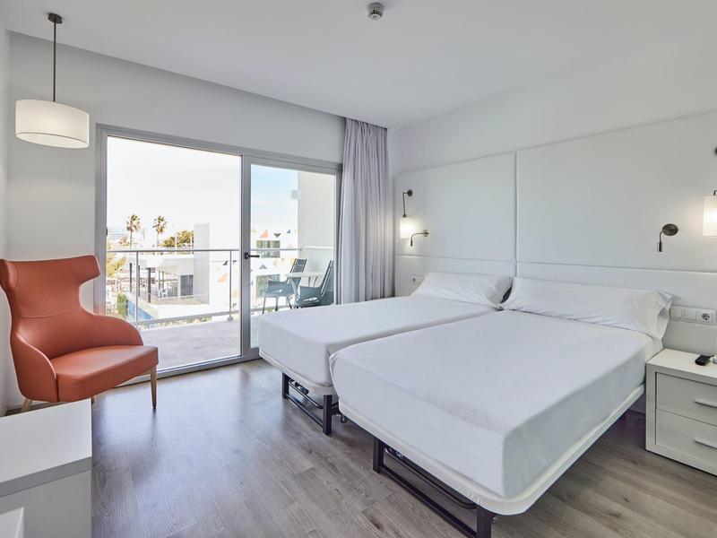 Habitación de hotel luminosa con dos camas individuales, diseño moderno y balcón con vista a la ciudad.