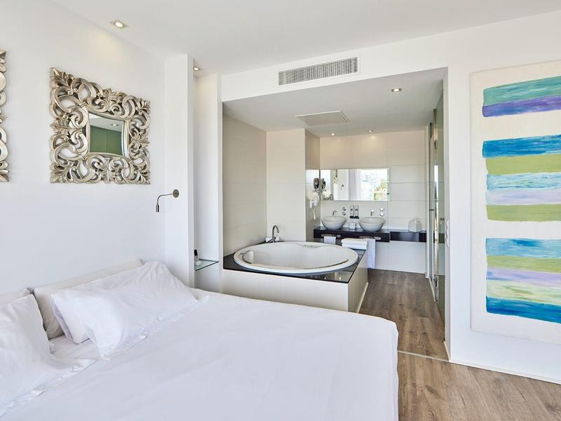 Dormitorio luminoso con cama doble, espejos decorativos y baño con bañera grande.