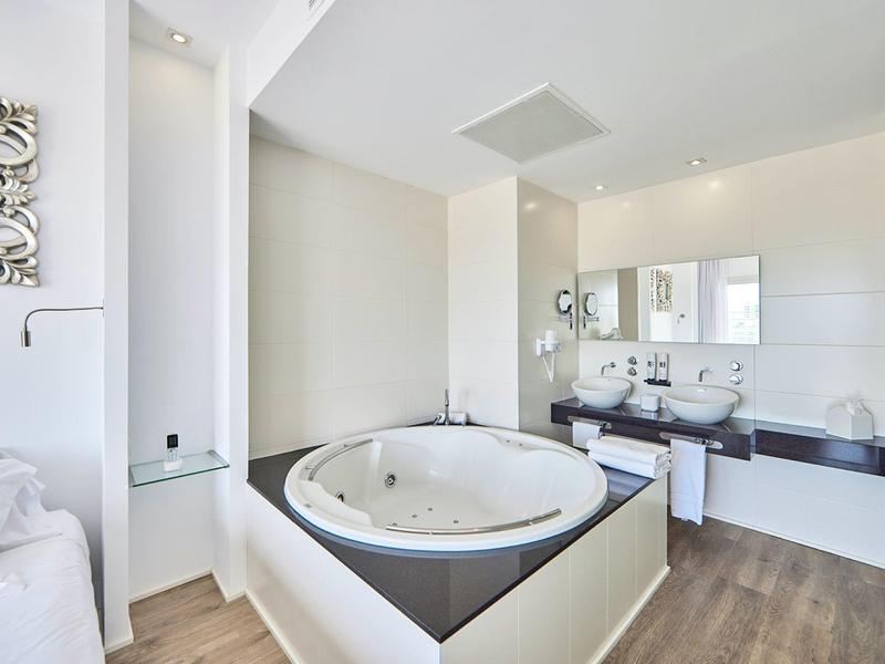 Baño moderno con gran bañera redonda, lavabo doble y suelo de madera