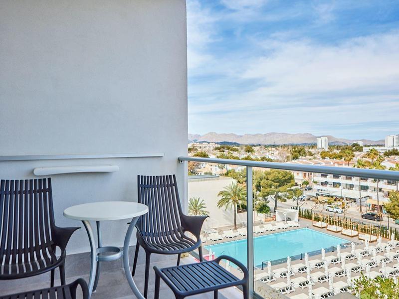 Balcón con dos sillas y mesa pequeña con vista a una piscina y complejo hotelero.