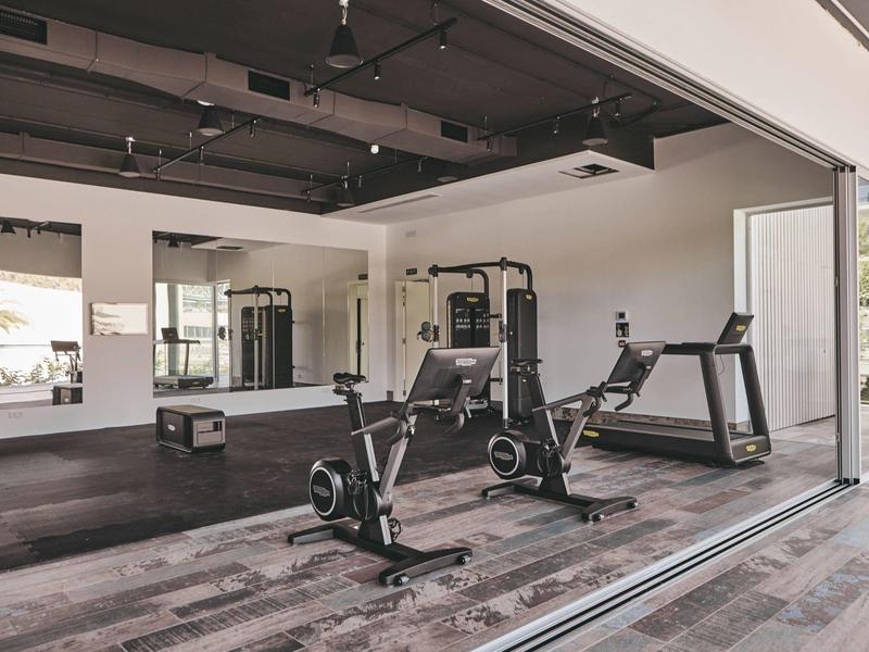 Gimnasio moderno con equipos de entrenamiento, cinta de correr y grandes ventanas para luz natural.