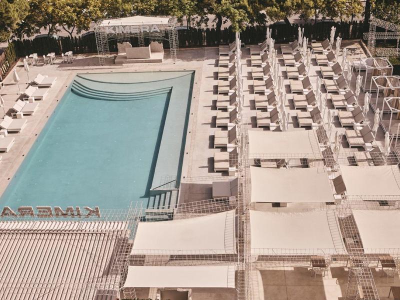 Vista de una piscina exterior rectangular con filas de tumbonas y sombrillas a un lado.