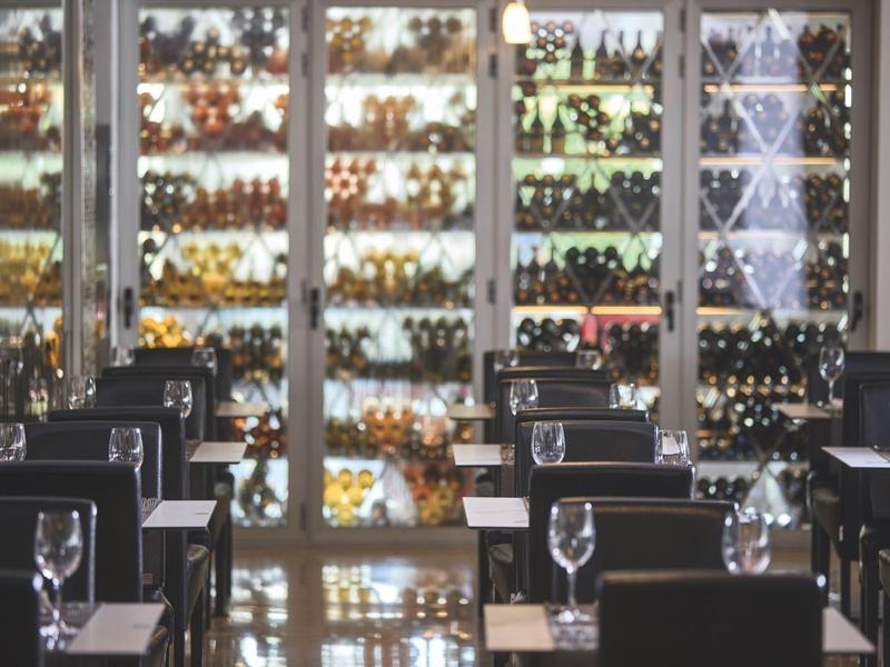 Elegante área de comedor con manteles y copas frente a una vitrina bien surtida de vinos.