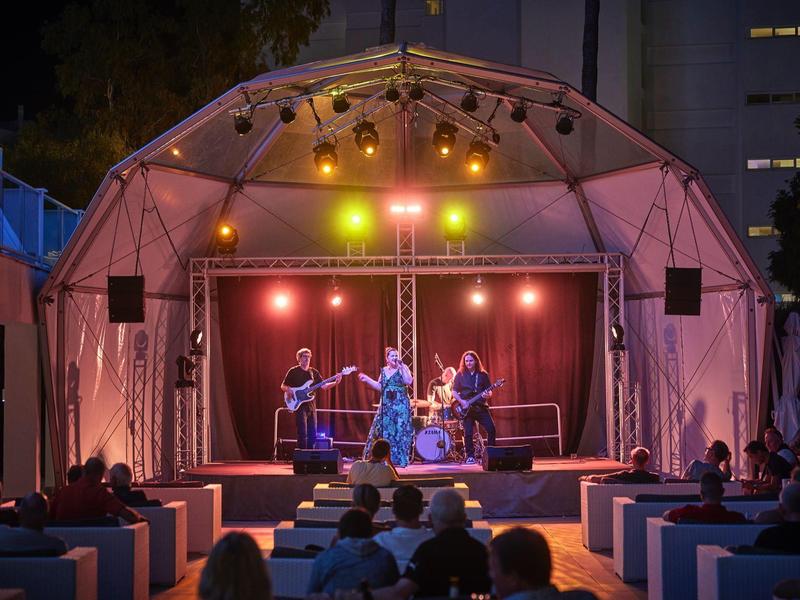 Escenario iluminado con músicos en un evento nocturno al aire libre frente a la audiencia.