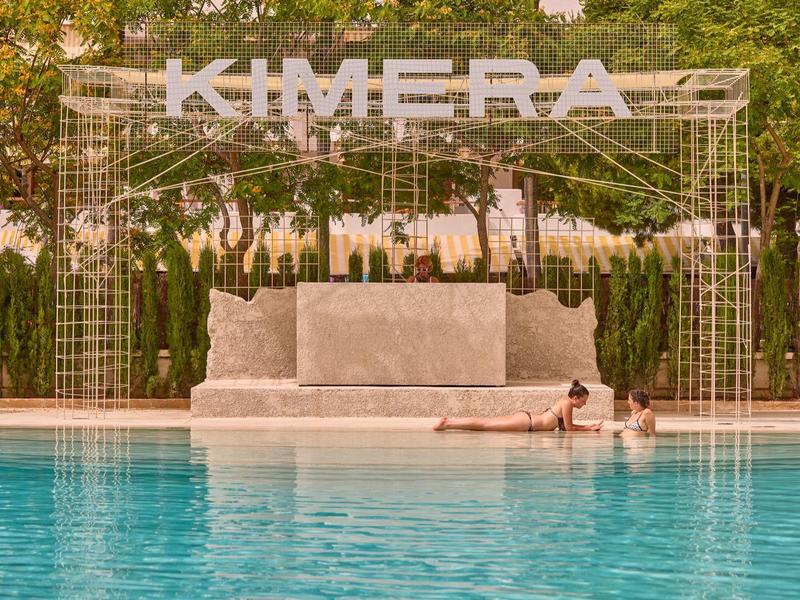 Una piscina moderna con un letrero blanco de Kimera y dos personas en el agua.