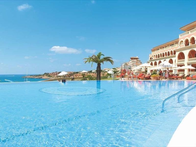 Large pool with sea view, surrounded by hotel buildings and sun umbrellas.
