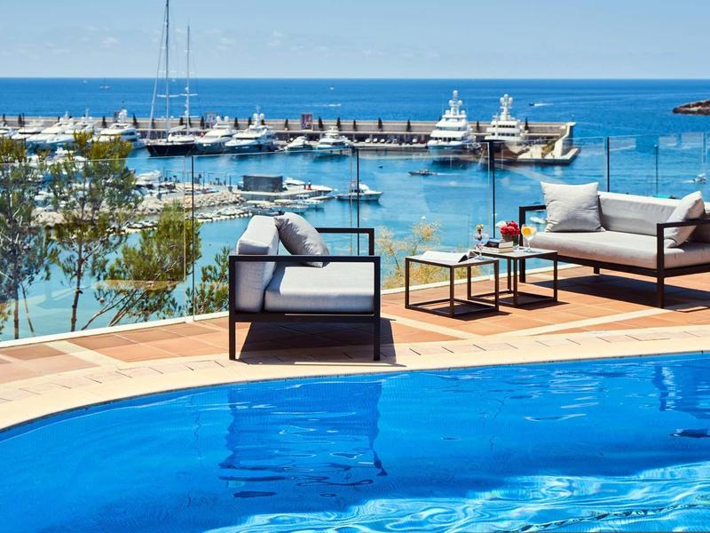 Terrace with modern seating furniture overlooking a marina and the sea.