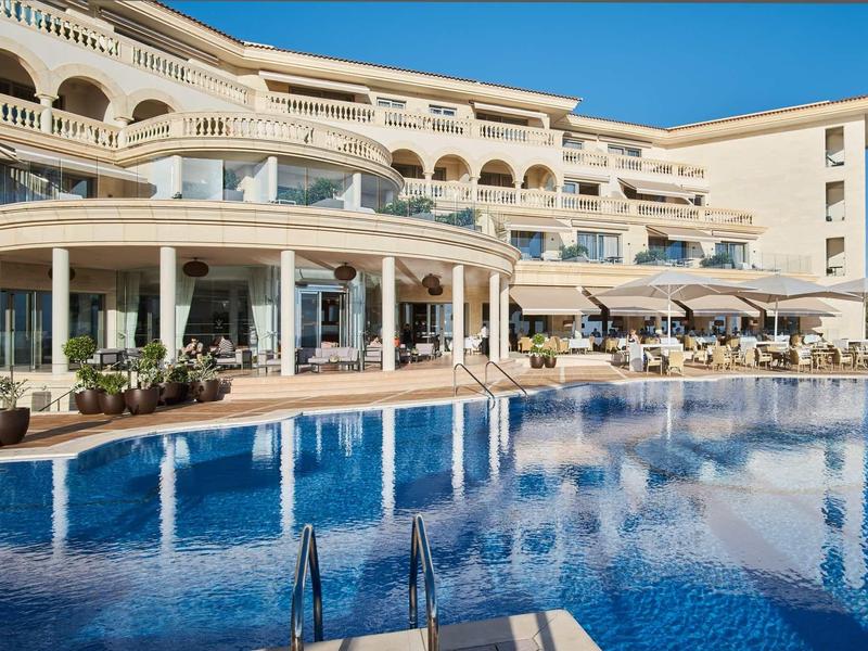 Modern hotel complex with outdoor pool and umbrellas under clear sky.