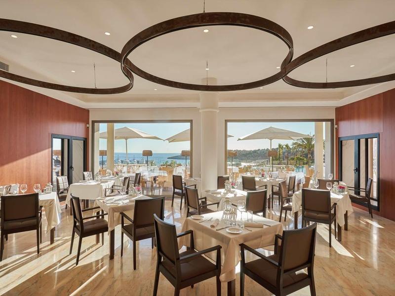 Elegant restaurant with wooden chairs and tables, view of pool and sea on a clear day.