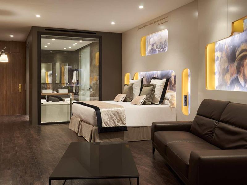 Modern hotel room with double bed, sofa, and illuminated wall art.