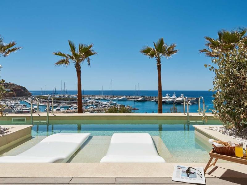 Luxurious pool area with loungers, palm trees, and view of the marina in sunlight.