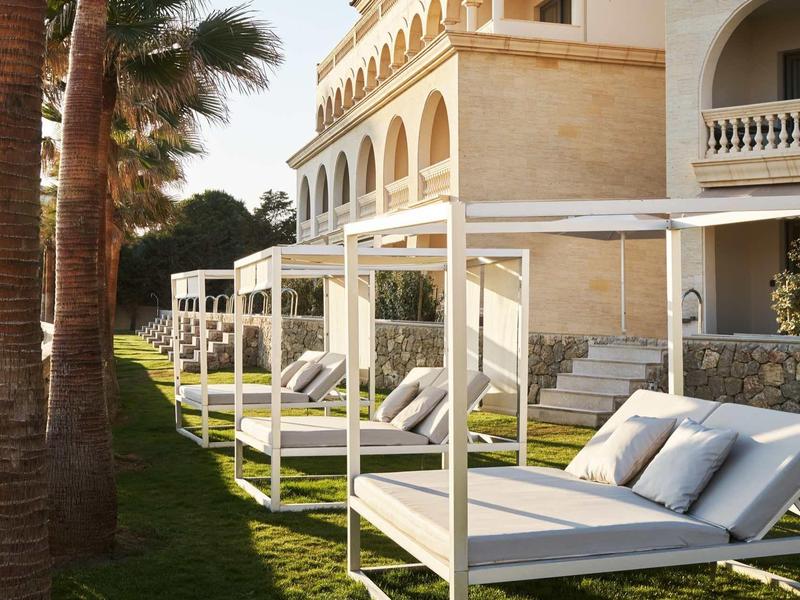 White sun loungers with canopies beside a hotel building in sunny garden
