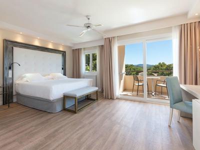 Modern hotel room with large bed, balcony, and nature view.