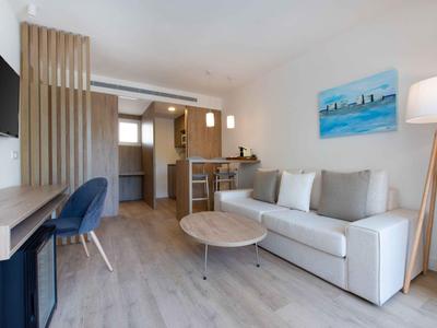 Modern hotel room with sofa, dining table, workspace, and kitchen in bright design.