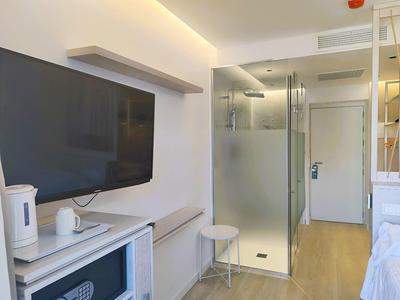 Compact hotel room with wall-mounted TV, kitchenette, and glass shower in modern style.