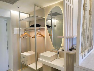 Bright hotel room closet with open shelves, oval mirror, and hanging hangers