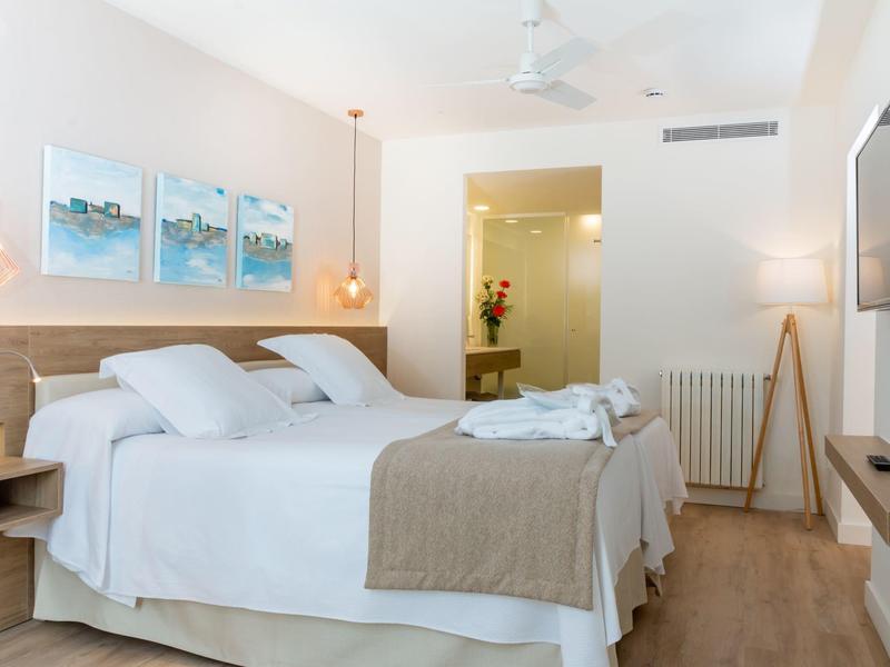 Modern hotel room with two beds, white bedding, and light wooden furniture.