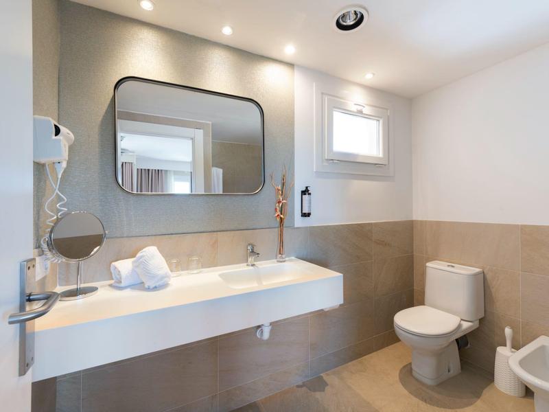 Bright bathroom with large mirror, sink, toilet, and bidet in neutral tones.