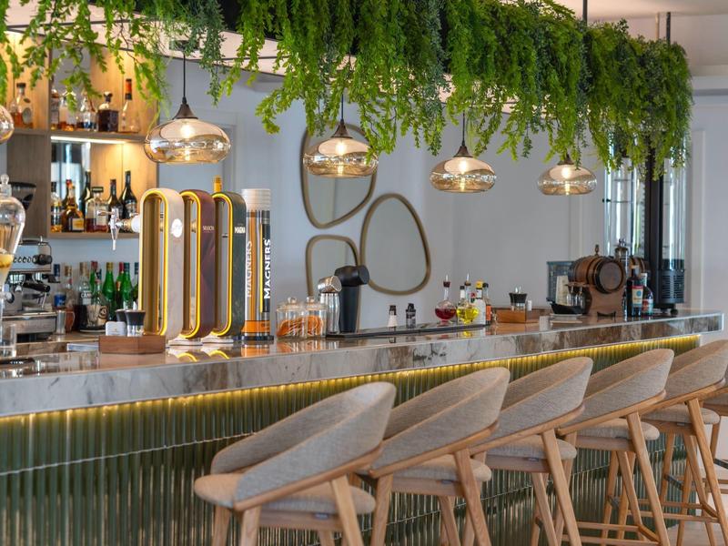 Modern bar with light wooden stools and hanging plants above the counter.