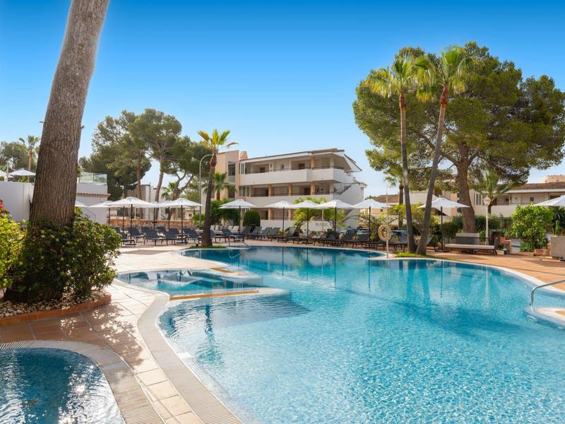 Large outdoor pool with sun umbrellas and multi-story hotel building in the background.