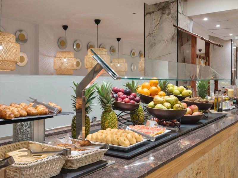 Buffet with fresh fruits, pastries, and bread baskets in a modern hotel restaurant.