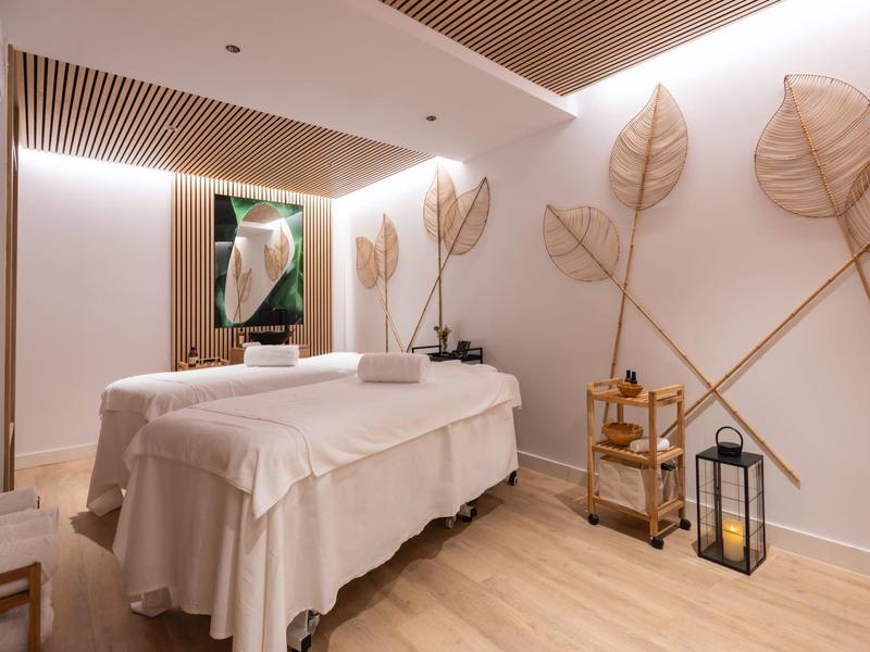 Bright massage room with soft treatment tables and delicate leaf-shaped wall decorations.
