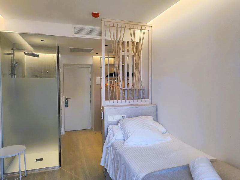Single room with a simple bed, white bedding, wooden partition, and modern bathroom door.