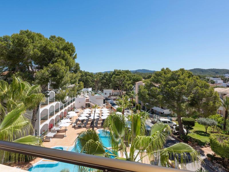View of a sunny hotel pool area with lounge chairs and surrounding trees.