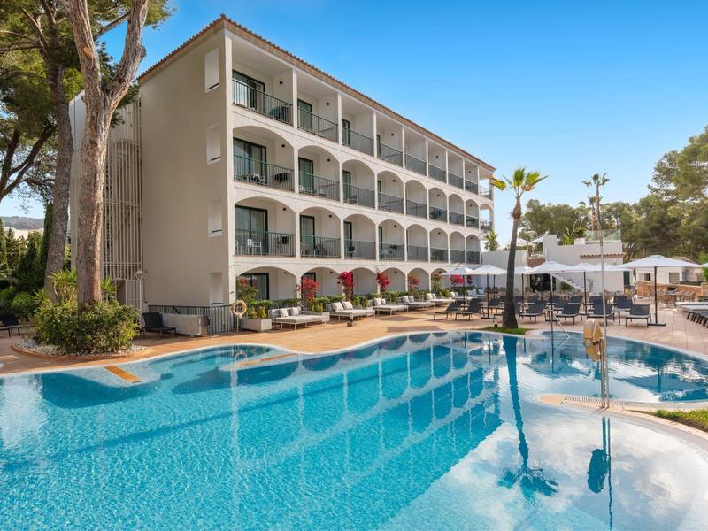 Multi-story hotel building with balcony rooms next to a large pool with sun loungers.