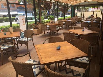 Overdekt terras met houten tafels en rieten stoelen in een café of hotel.