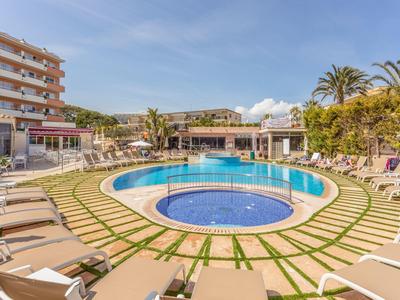 Runder Swimmingpool mit Liegestühlen und Palmen in einem Hotelgarten unter blauem Himmel.