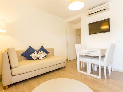 Modern eingerichtetes Wohnzimmer mit beigem Sofa, blau-weißen Kissen, Esstisch und Wandfernseher.