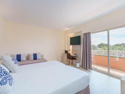 Helles Hotelzimmer mit zwei Betten, Schreibtisch, Fernseher und Balkon mit Aussicht.