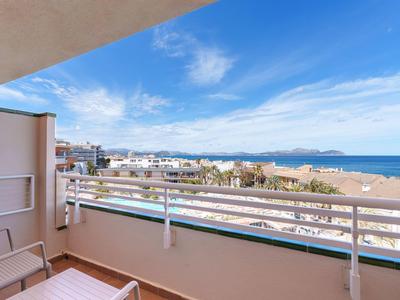 Balkon mit Stühlen und Blick auf Strand, Meer und Stadt unter blauem Himmel.