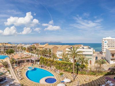 Blick auf ein Hotel mit mehreren Schwimmbädern und Meer im Hintergrund unter blauem Himmel.