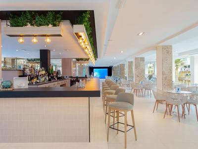 Heller, moderner Hotelbar- und Speisesaal mit Barhockern und Tischen in neutralen Farben.