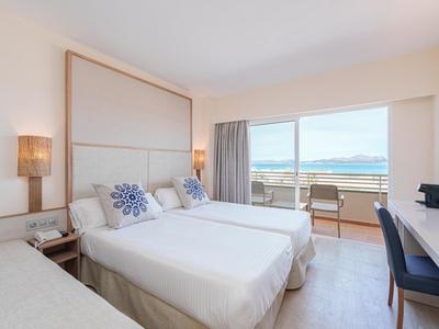 Hell eingerichtetes Hotelzimmer mit zwei Einzelbetten und Balkon mit Meerblick.