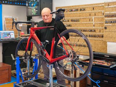 Mann repariert rotes Rennrad in einer Werkstatt mit Werkzeugwand im Hintergrund.