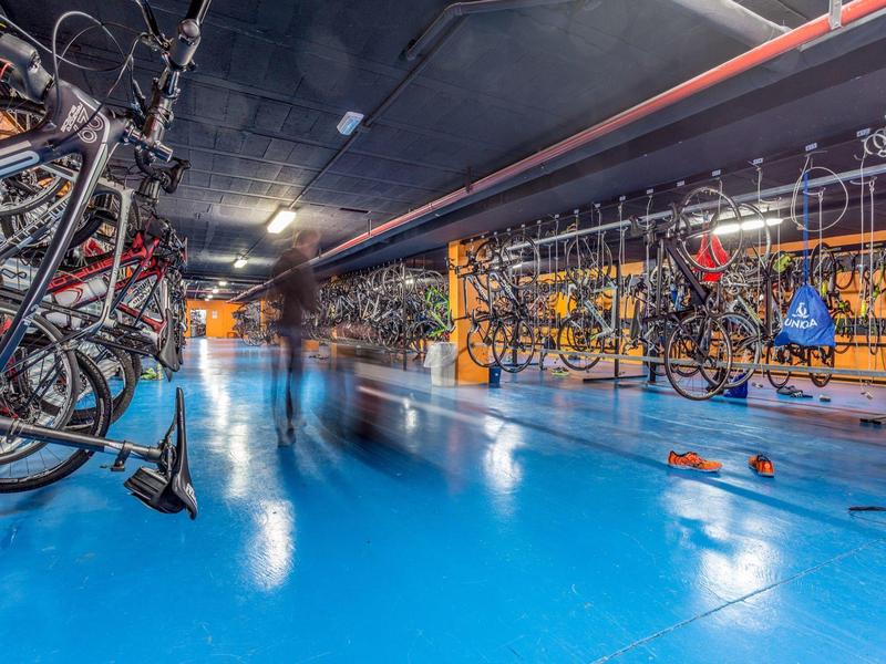 Fahrradparkplatz mit vielen Fahrrädern und blauer Bodenbeschichtung in einem Gebäude.