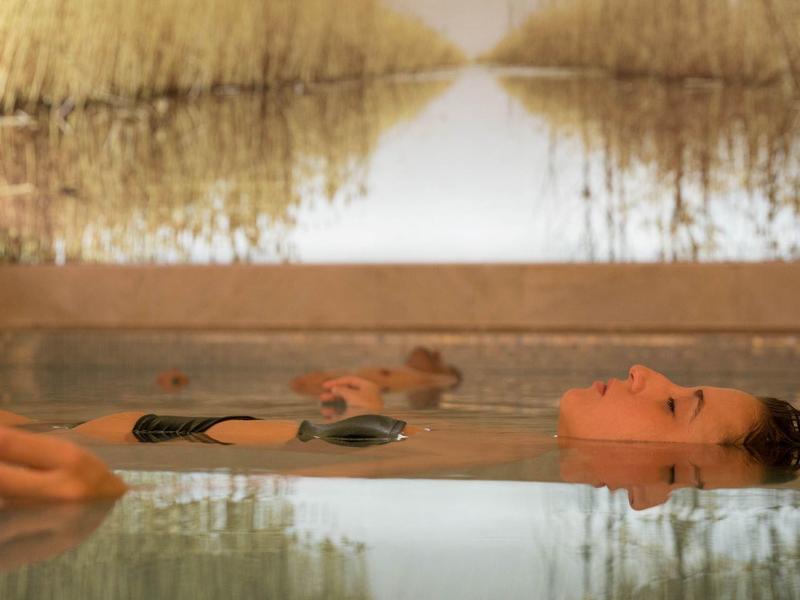 Frau entspannt sich im Wasser eines Pools mit ruhiger Atmosphäre und reflektiertem Hintergrund.