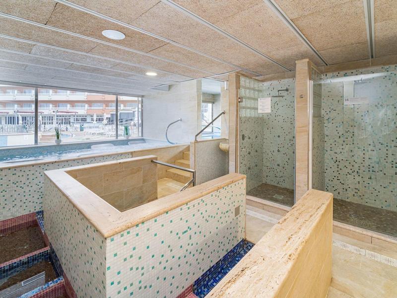 Saunabereich mit Holzverkleidung, Duschen und Sitzbänken neben großen Fenstern.