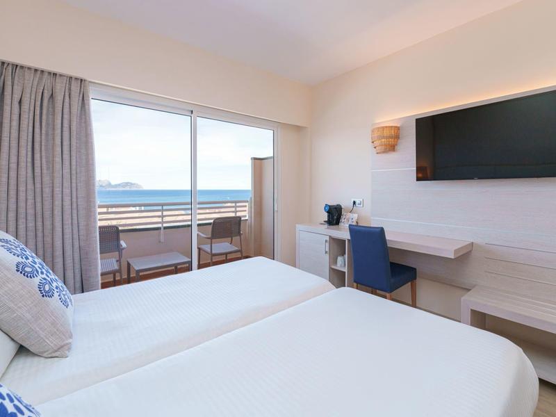 Modernes Hotelzimmer mit zwei Einzelbetten, Schreibtisch und Meerblick vom Balkon.