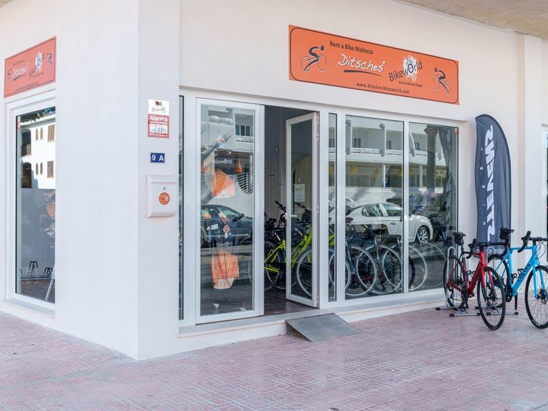 Moderne Fahrradverleihstation mit mehreren Fahrrädern vor einem weißen Gebäude.