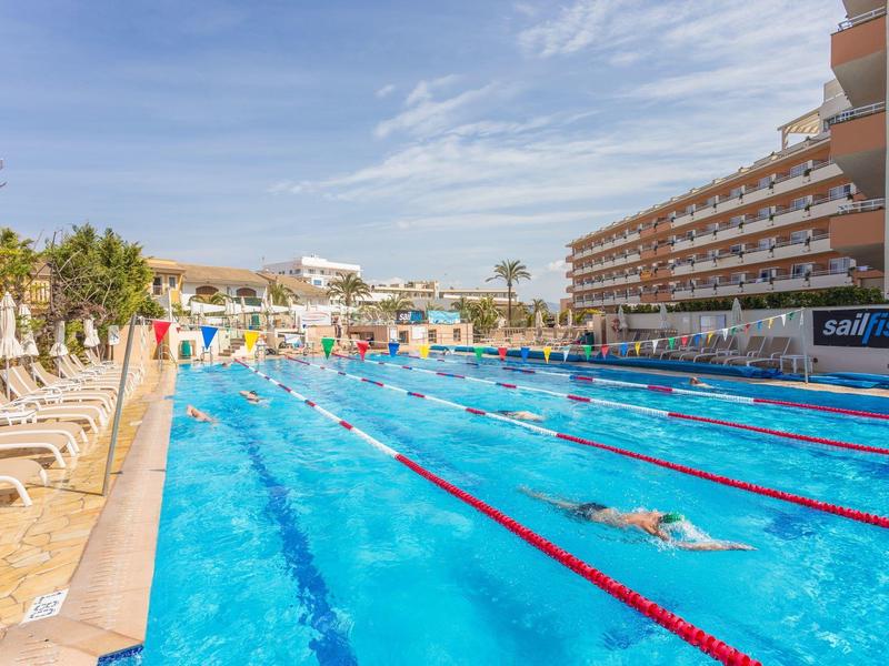 Großes Außen-Schwimmbecken mit Bahnen, Liegestühlen und Hotelgebäude im Hintergrund