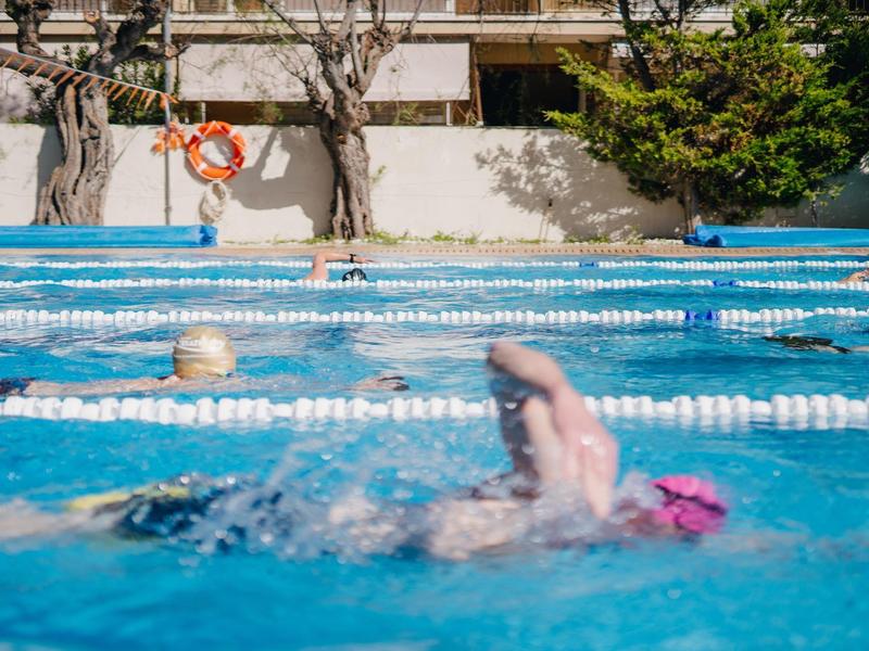 Schwimmer mit rosa Badekappe schwimmt in einem Außenpool mit Bahnen.