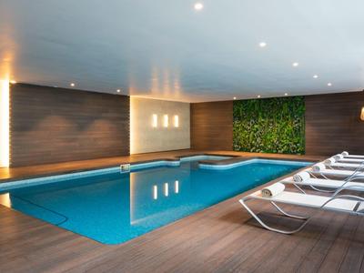 Hallenbad mit Liegestühlen und grüner Pflanzenwand in modernem Spa-Bereich.