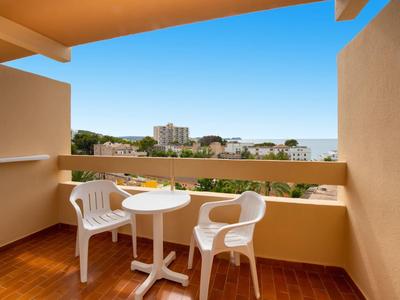 Balkon mit zwei weißen Stühlen und kleinem Tisch mit Blick auf Stadt und Meer.