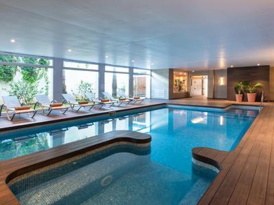 Innenpool mit Holzterrasse, Liegestühlen und großen Fenstern mit Blick ins Grüne