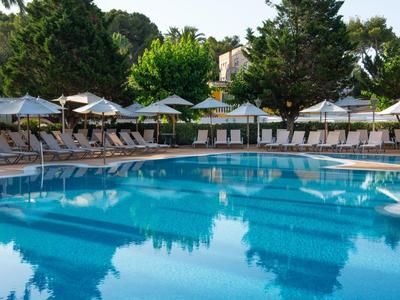 Großer Außenpool mit Liegestühlen und Sonnenschirmen, umgeben von Bäumen.